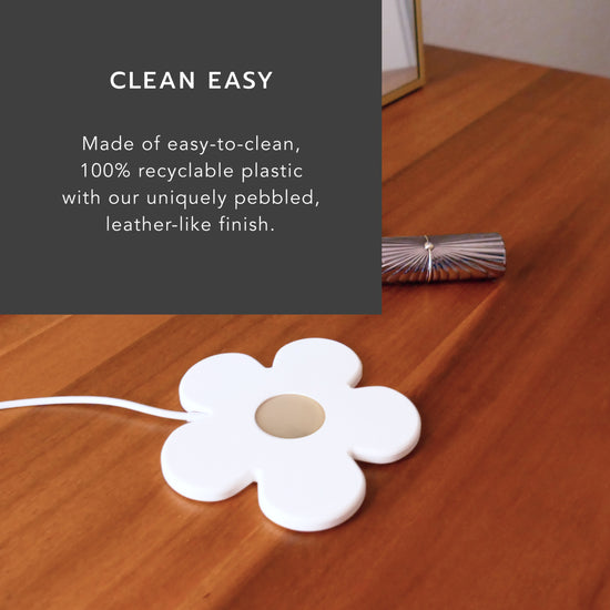 Image: Floral shaped charger next to lipstick on wooden Mid-Century modern dresser. Gold frame mirror in background. Heading: Clean easy. Body text: Made of easy-to-clean, 100% recyclable plastic with our uniquely pebbled, leather-like finish. 