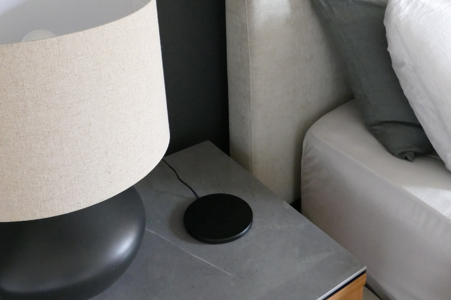 Image: Wood nightstand with black marble top styled with black sculptural lamp with beige and cream linen shade. Wireless charger on top with black case. 